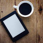 kindle e-reader on wooden table next to a cup of coffee