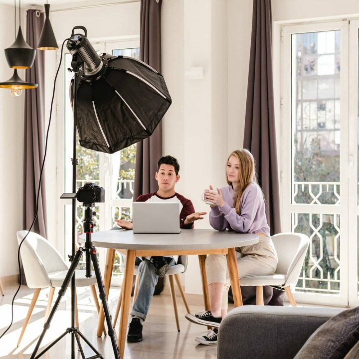 man and woman in casual clothes at dining table filming a podcast